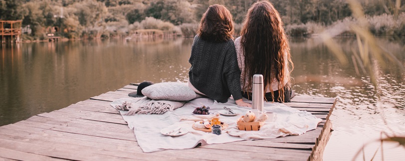 two women sat at a lake in autumn 