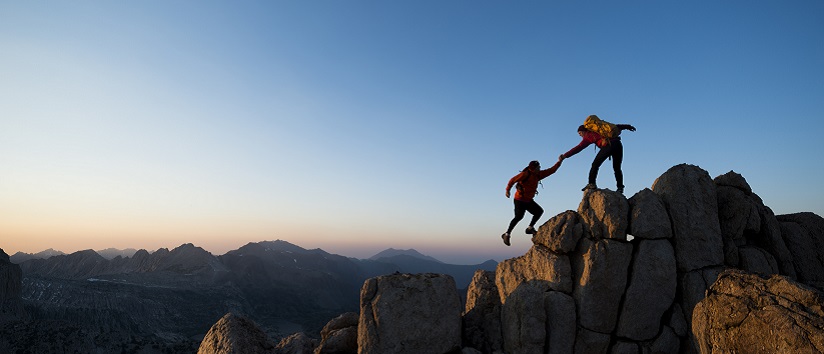 friends mountain climbing, one reaches down to help the other