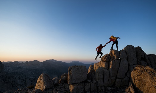 friends mountain climbing, one reaches down to help the other