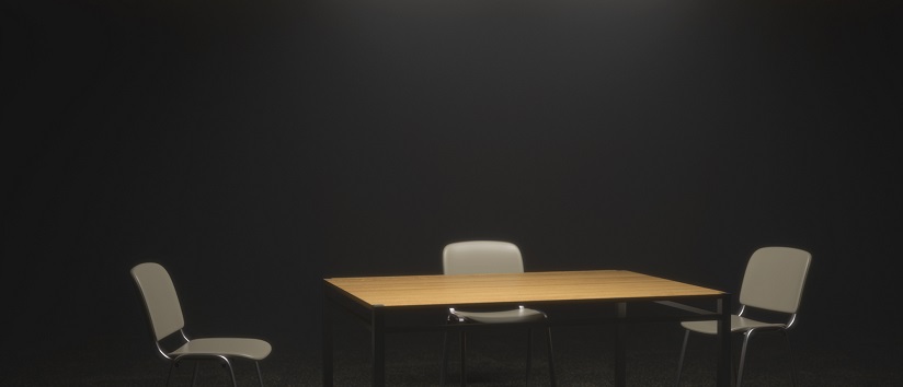an interrogation room mostly in shadow with a light illuminating a table and two chairs