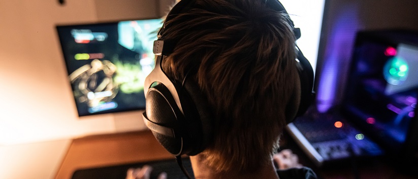 back of young mans head wearing gaming headphones, he is staring at a screen and holding a controller