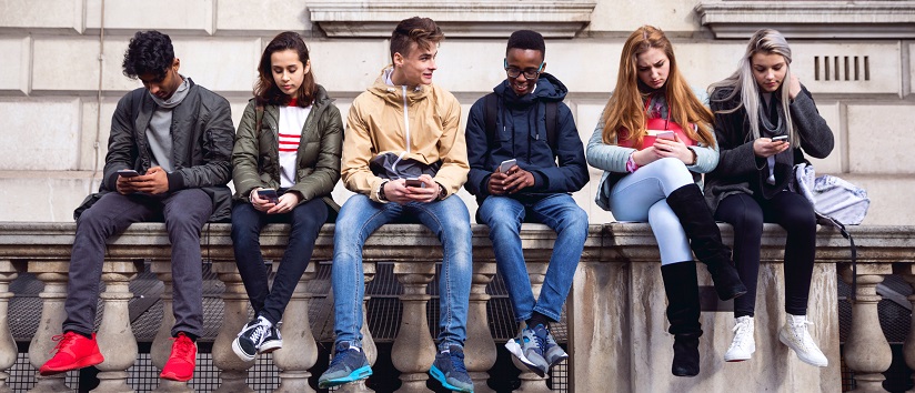 group of diverse young people sat together on a wall looking at their phones