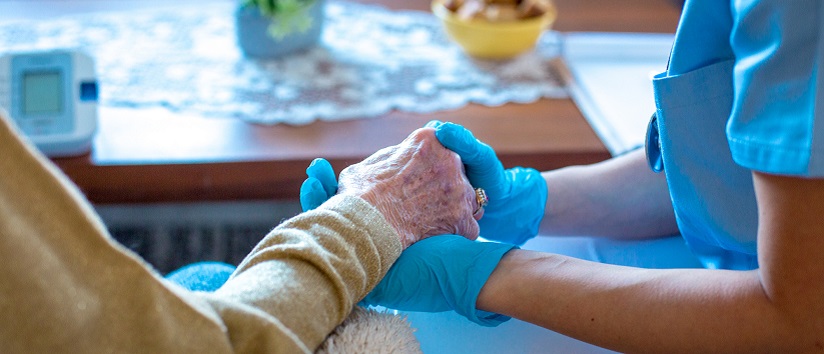 a care worker in scrubs holds the hand of an elderly woman